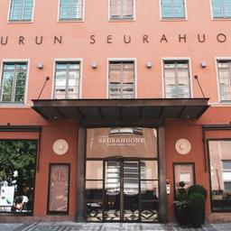 The light pink exterior of Turun Seurahuone, featuring four flags and the words 'Turun Seurahuone' on the wall.