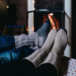 Two pairs of entwined feet in woolen socks relax beside the fire at Meripesä Holiday Village.